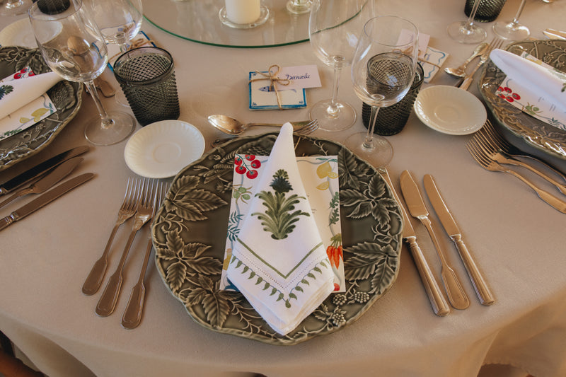 Dining table setting with decorative plates, napkins, menu and cutlery on a white tablecloth.