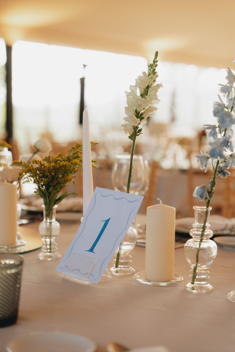 Wedding table setting with flowers, candles, and a table number card on a blurred background