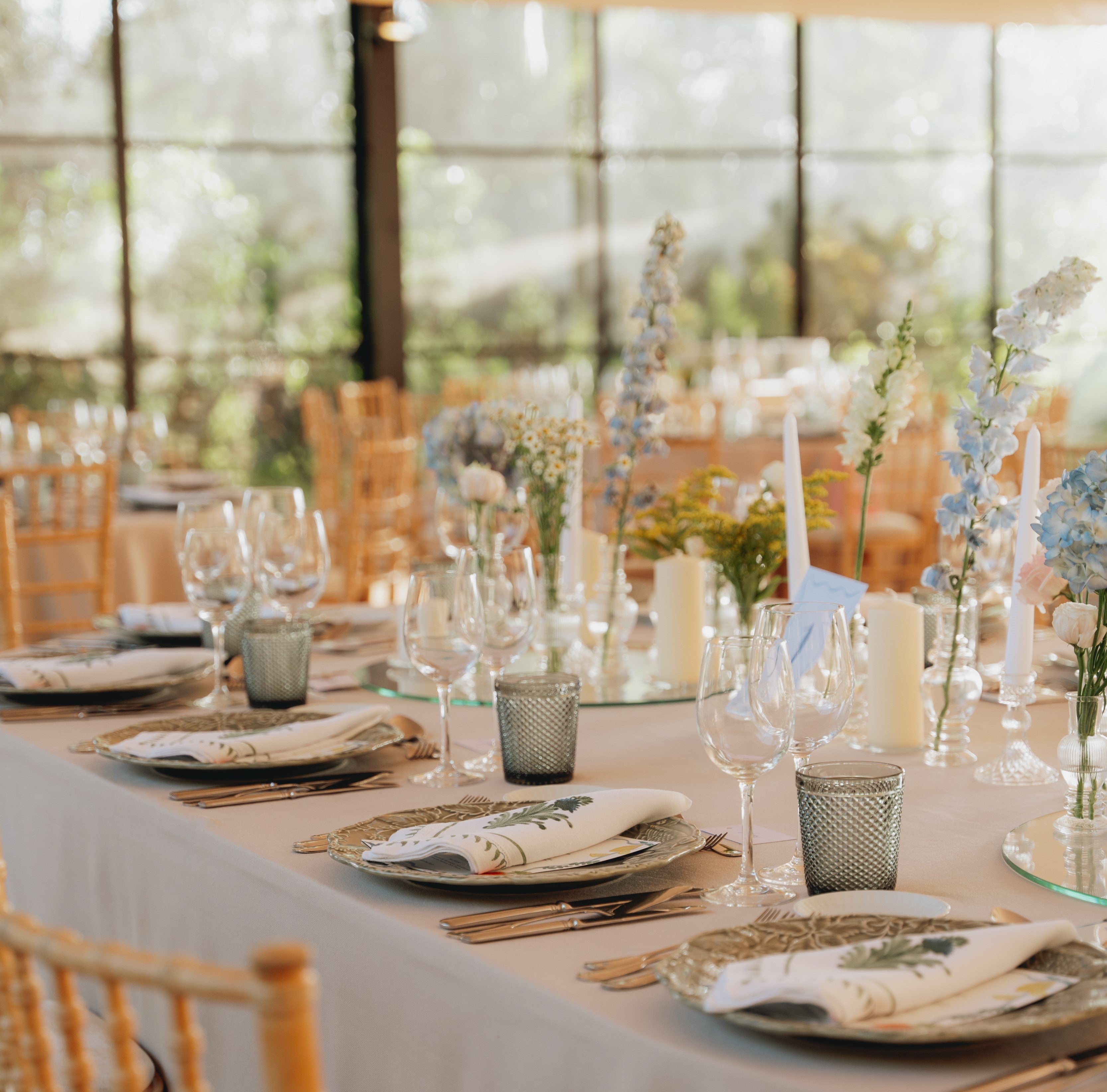 Elegant  wedding table setting with floral centerpieces in a room with large windows.