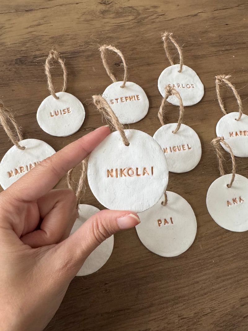 Hand holding a clay name tag with 'Nikolai' on a wooden surface with other name tags.
