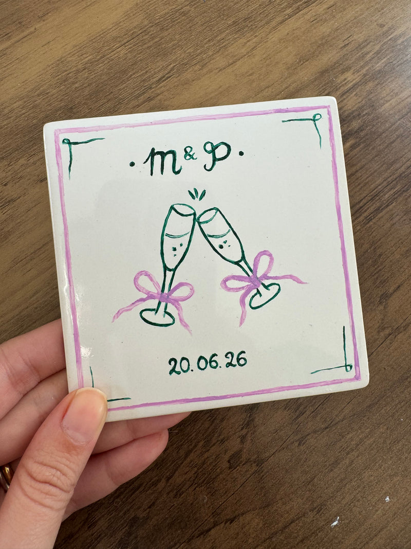 Handpainted tile or coaster with champagne glasses, initials and  wedding date, held by a hand.