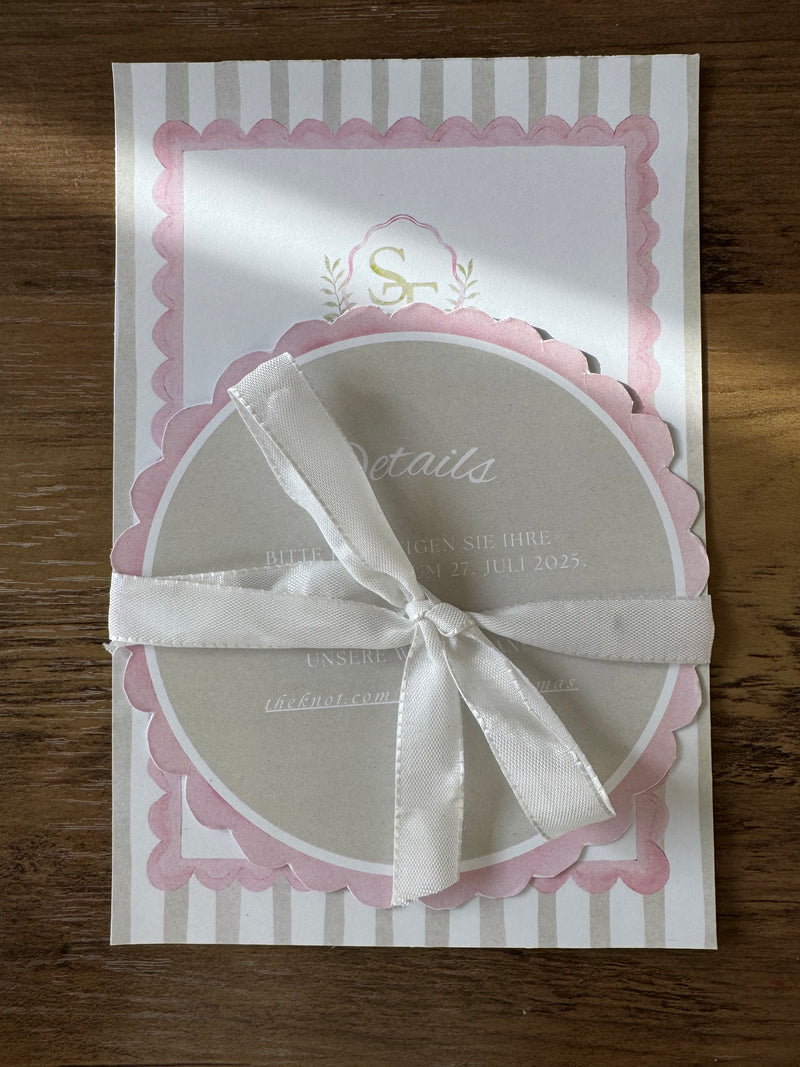 Wedding invitation with two cards and a white ribbon, placed on a wooden surface.