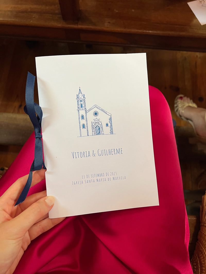 Ceremony program with blue illustration of a church, held by a person.
