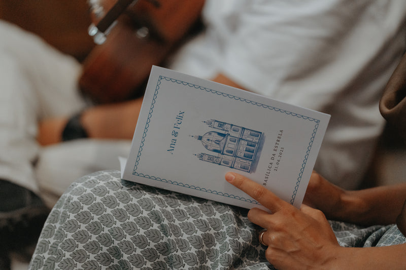 Person holding a ceremony program with a blue basilica illustration, blurred background