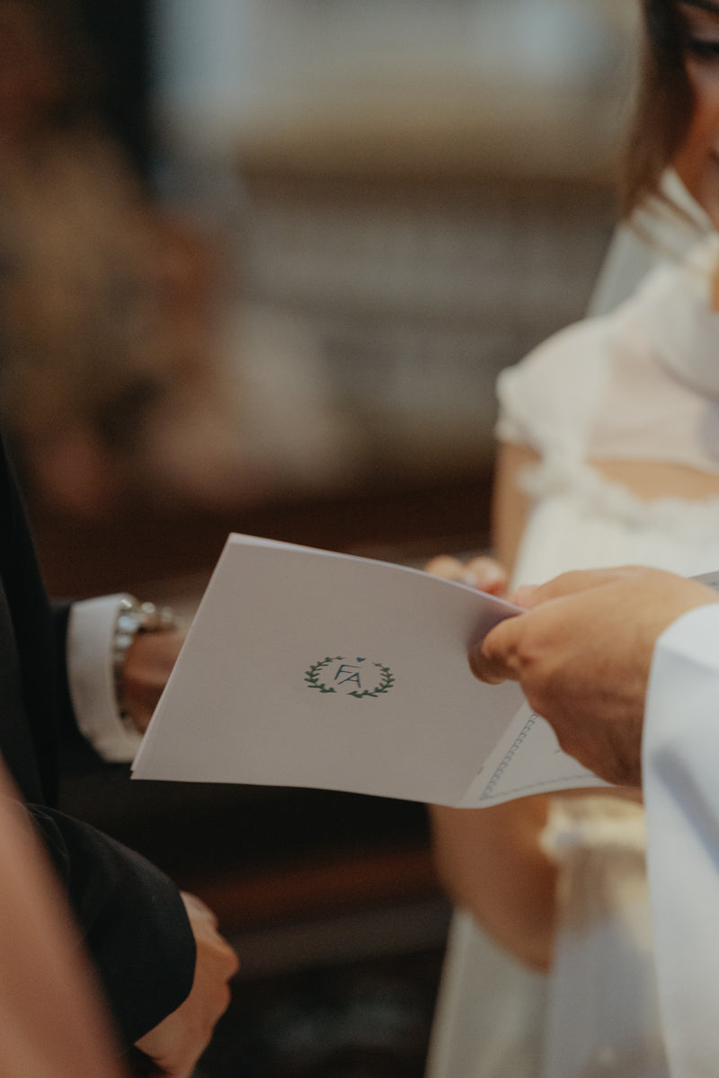 Person holding a ceremony program with a handpainted monogram with the couples initials.