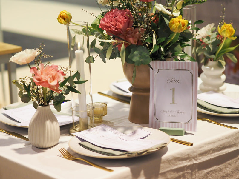 Decorative table setting with flowers, candles, a menu and a table number card.
