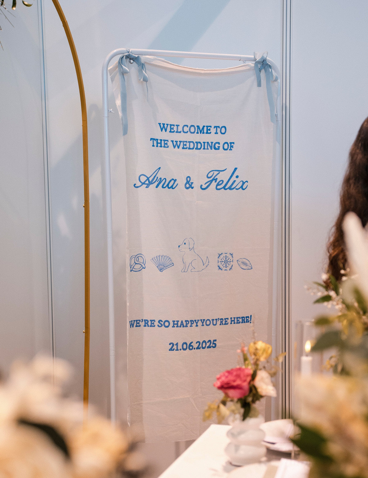 Wedding welcome sign with names, wedding date and illustrations, surrounded by floral decorations.