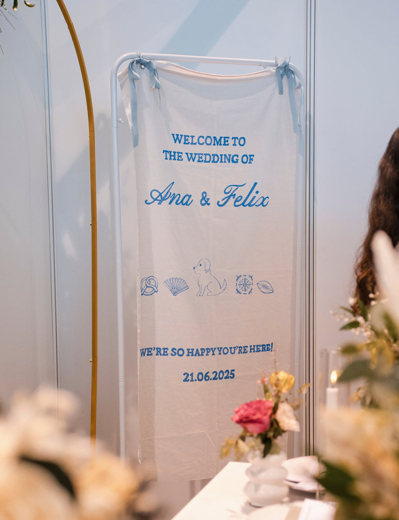 Wedding welcome sign with names, wedding date and illustrations, surrounded by floral decorations.