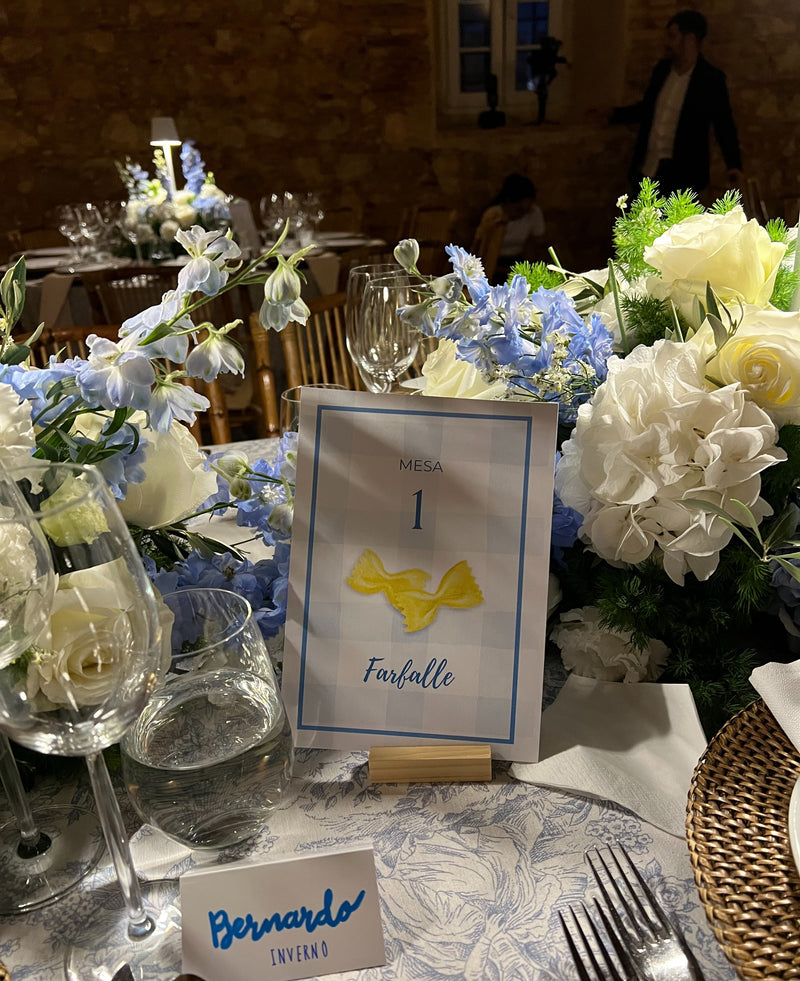 Decorated wedding table with floral arrangements and a table number card with a farfalle illustration.